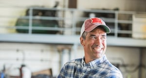 Man in his mid 40s wearing a plaid shirt and trucker hat about the replace a compact tractor cylinder